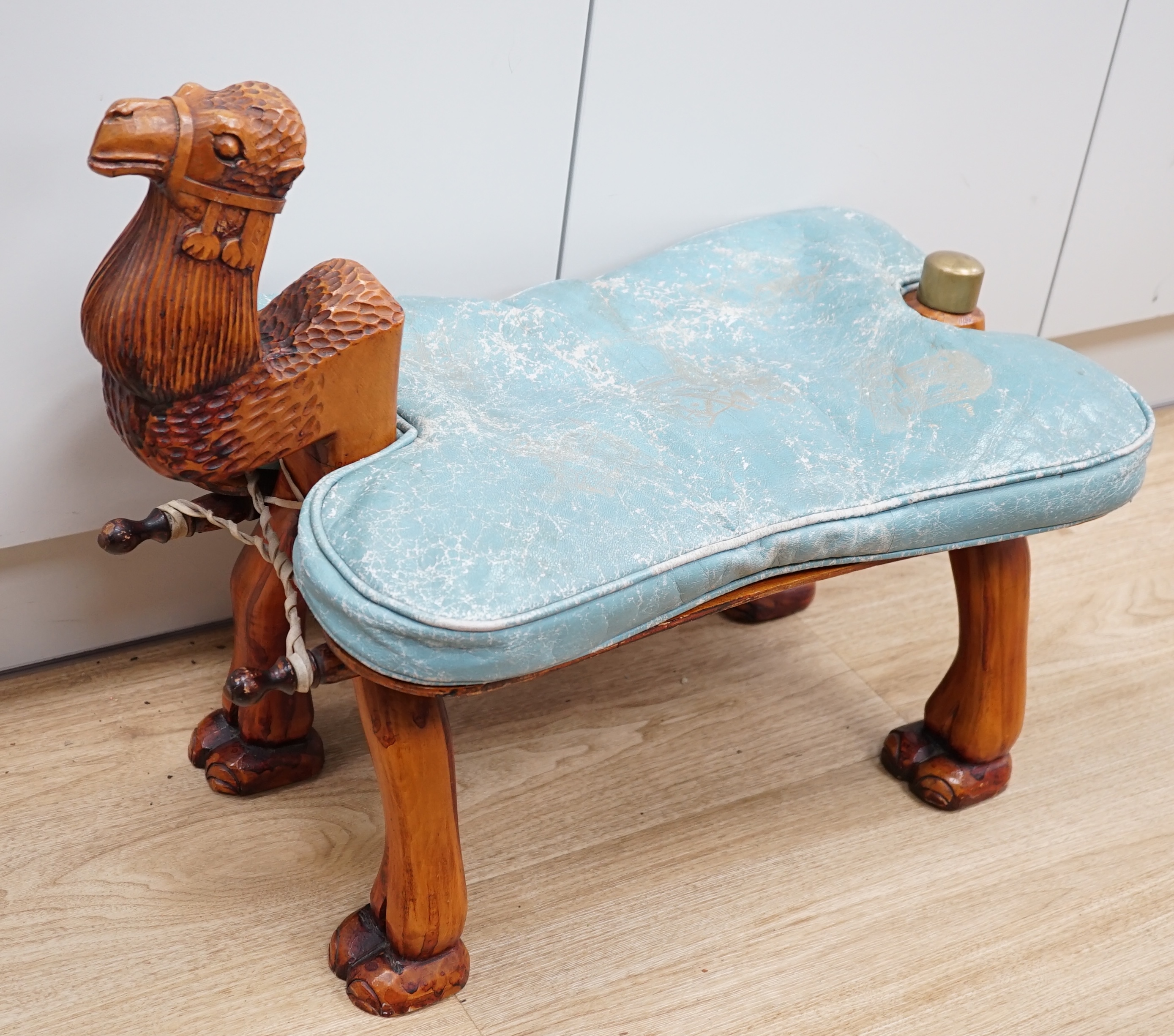 A carved wood foot stool in the form of a camel, blue stamped patterned leather cushion, 56cm high, 71cm wide. Condition - frame good, leather cushion worn